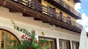 A building with a yellow facade, wooden balconies, and a stone wall with potted plants. - Life Hotels Des Alpes (Folgaria)