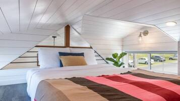 A bedroom with a sloped ceiling, a bed with a striped bedspread, and a view of parked cars through a window.
