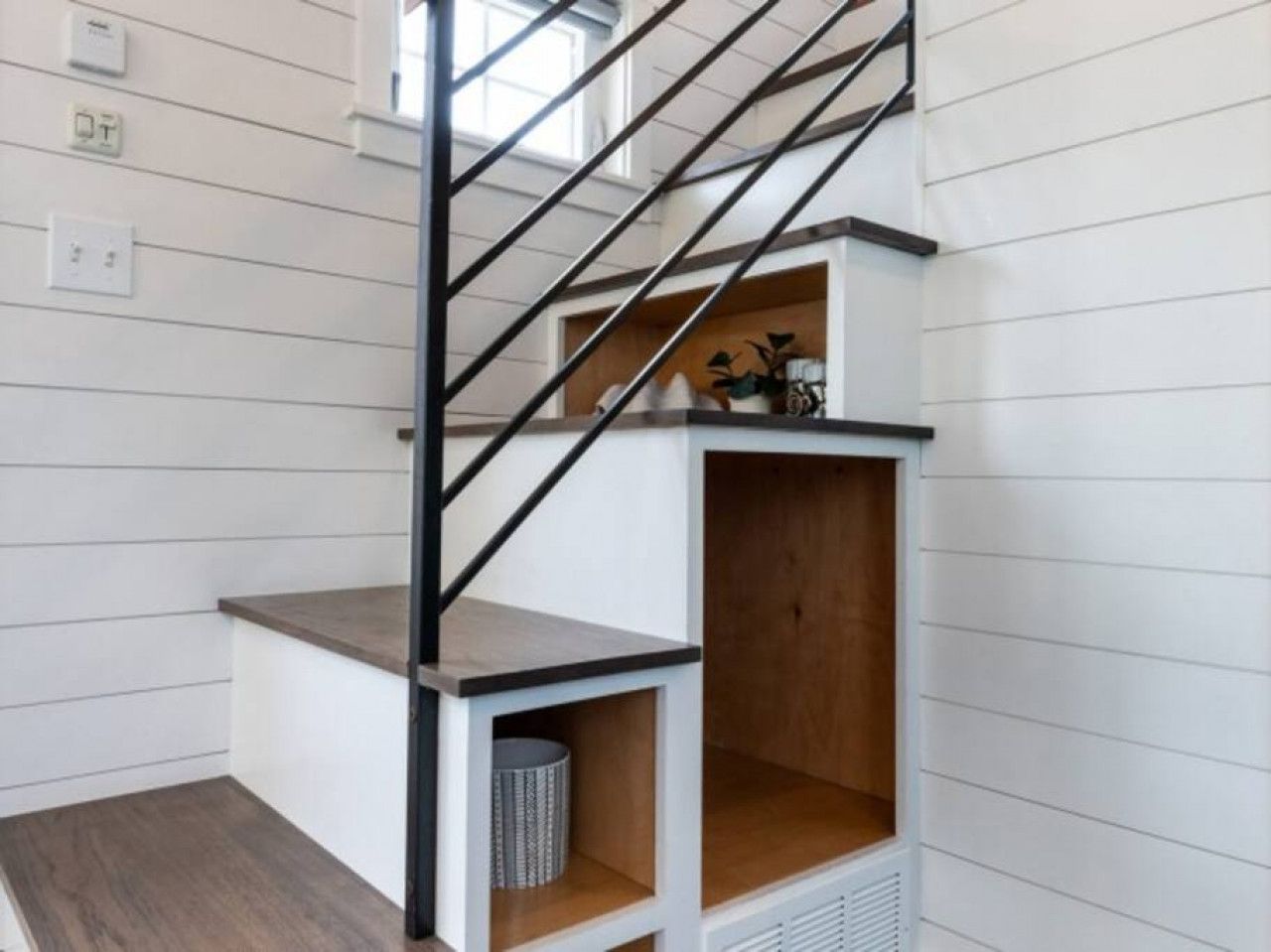 A staircase with a metal railing, a wooden shelf, and a trash can.