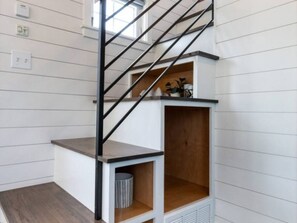 Eine Treppe mit Metallgeländer, einem Holzregal und einem Mülleimer.