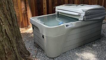 A portable hot tub with a cover, placed on gravel ground, next to a wooden fence.