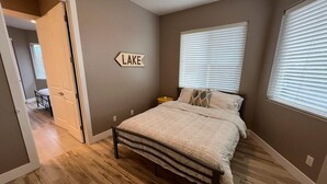A bedroom with a bed, a nightstand, a wall sign, and a door leading to another room.