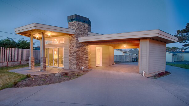 A modern two-story house with a stone chimney, large windows, and a covered patio area.