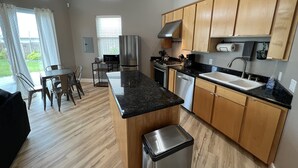 A modern kitchen with wooden cabinets, a black countertop, stainless steel appliances, and a dining area with a table and chairs.