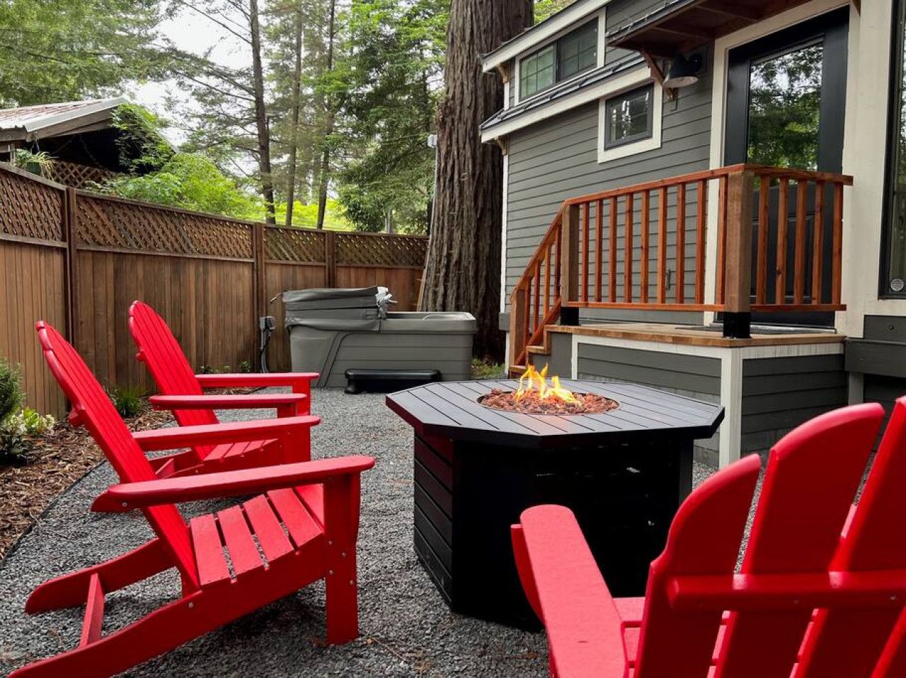 Une terrasse avec des fauteuils Adirondack rouges, un foyer et un escalier en bois menant à une maison.