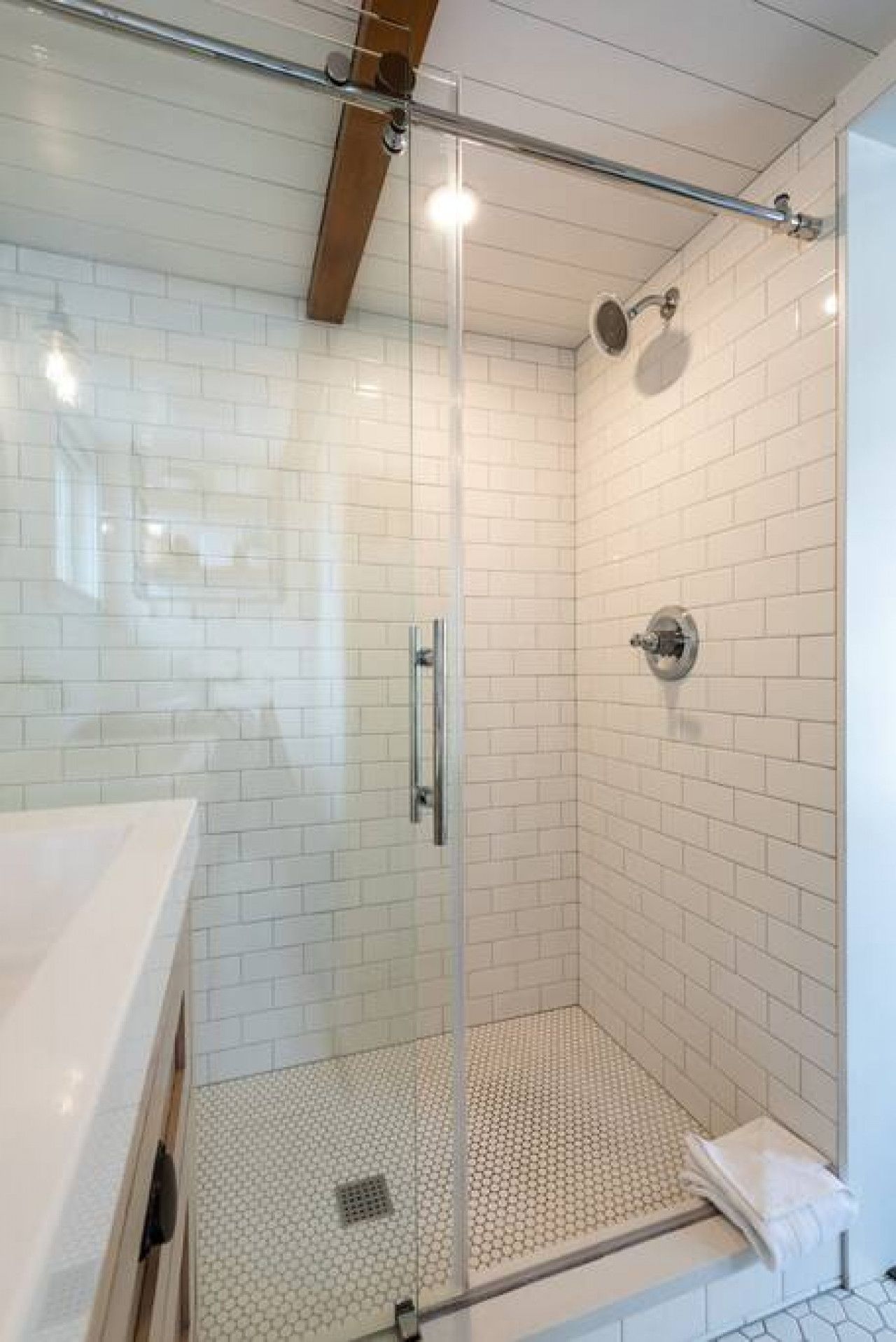 A glass-enclosed shower with white tiled walls and a white countertop.