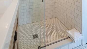 A glass-enclosed shower with white tiled walls and a white countertop.