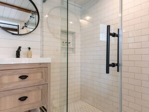 A modern bathroom with a glass shower enclosure, a wooden vanity with drawers, and a mirror above the vanity. - Tranquil Redwood Retreat (Guerneville)