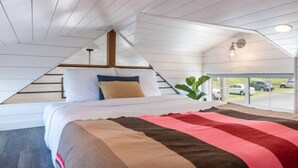 A bedroom with a sloped ceiling, a bed with a striped blanket, and a view of parked cars through a glass door.