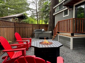 Un patio trasero con un pozo de fuego, sillas Adirondack rojas y un jacuzzi.