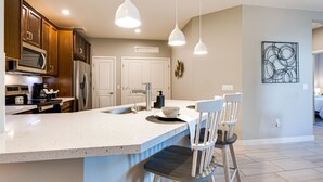 Cocina moderna con una isla grande, electrodomésticos de acero inoxidable e iluminación colgante.