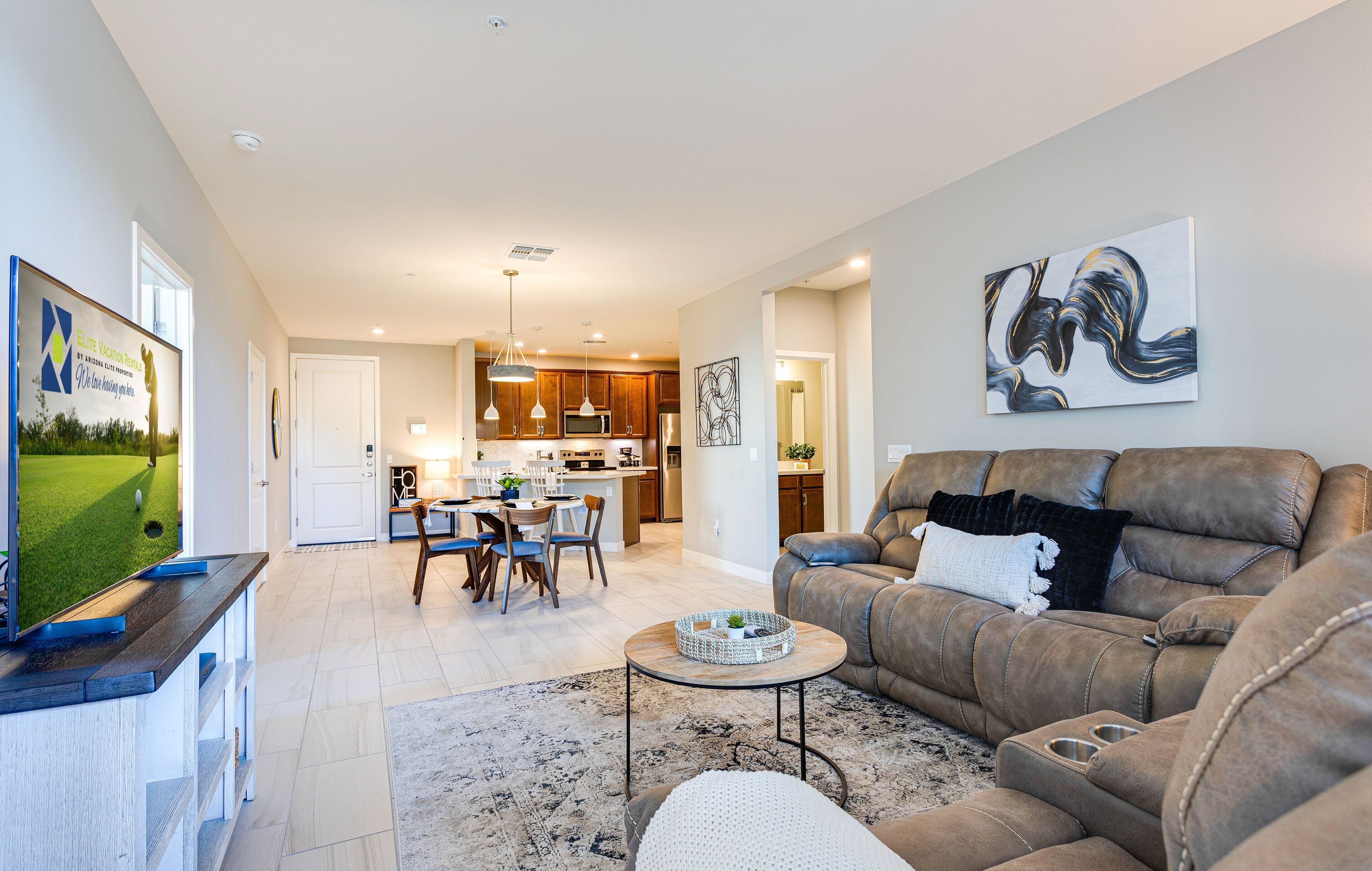 A modern living room with a leather sofa, a dining area with a table and chairs, and a kitchen in the background.