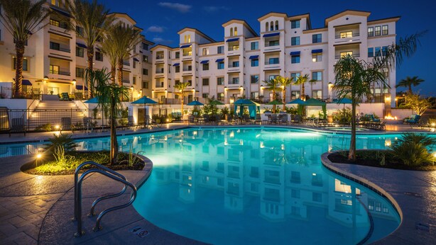 Un hotel con piscina, mobiliario exterior y palmeras.