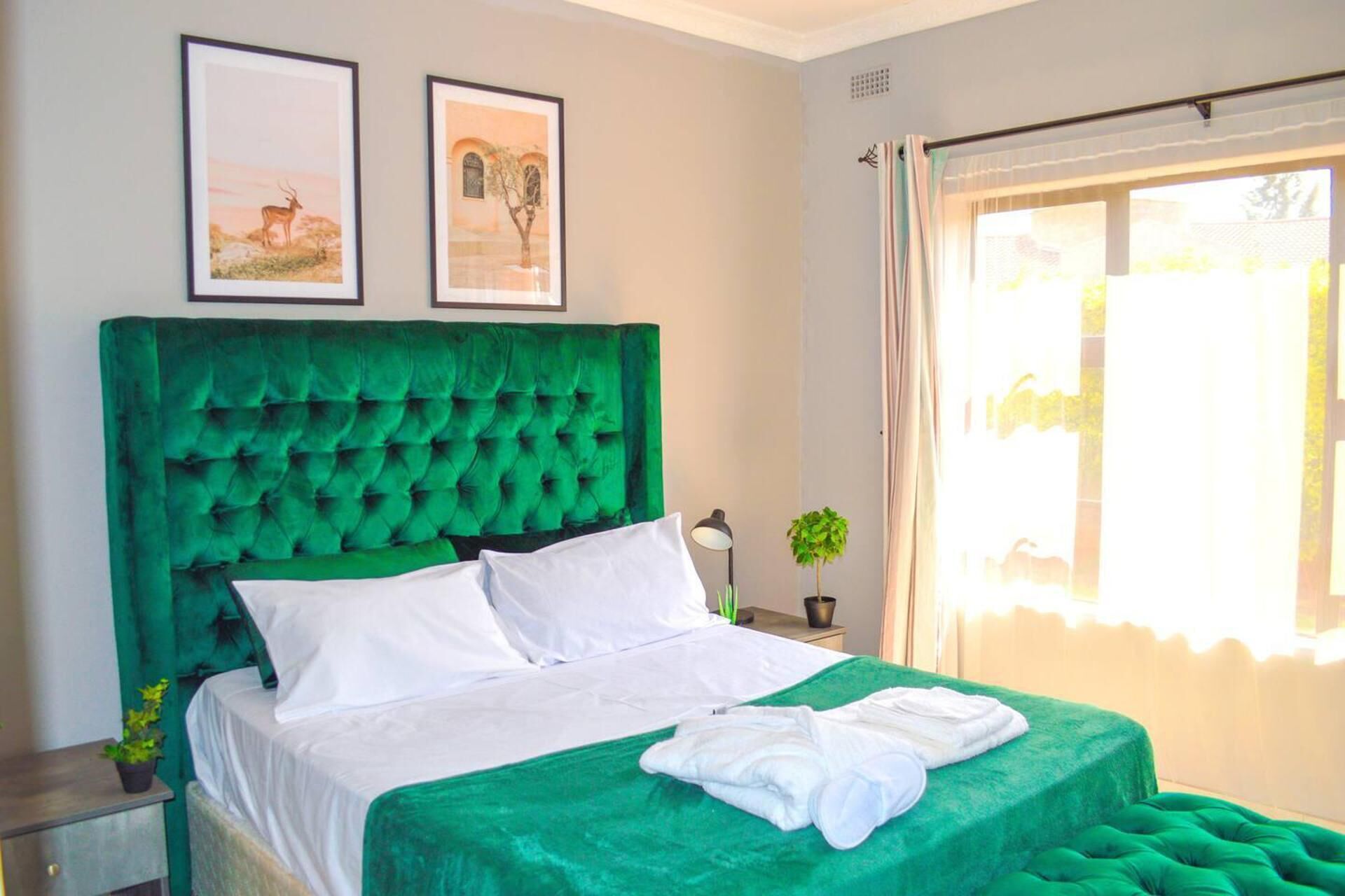 A neatly made bed with a green upholstered headboard, white linens, and a green throw blanket. There are two framed pictures on the wall above the bed.