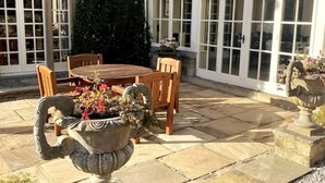 A patio with a round table and chairs, surrounded by stone flooring and large windows. - Exceptional Unique 5 Bedroom Manor House (Skipton)