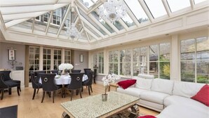 A conservatory with a glass ceiling, a dining area with a table and chairs, and a seating area with a sofa and cushions. - Exceptional Unique 5 Bedroom Manor House (Skipton)