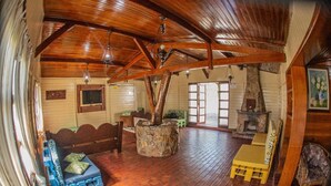 A spacious room with a high wooden ceiling, a stone fireplace, and a brick floor.