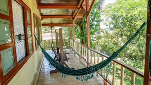 A covered porch with a hammock, wooden railings, and a view of greenery.