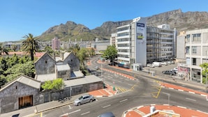 Eine Stadtansicht mit einem markanten Gebäude, das eine große Werbung zeigt, einer Kreisverkehr und einem Berg im Hintergrund.