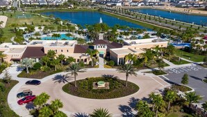 An aerial view of a resort with a central circular plaza, a large body of water, and multiple buildings with parking areas. - Solara Resort private POOL HOME 4 Bed (Kissimmee)