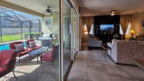 A spacious living area with a glass sliding door leading to a patio, a comfortable seating area, and a television in the background. - Solara Resort private POOL HOME 4 Bed (Kissimmee)