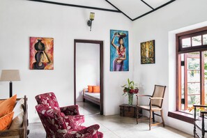 A room with a bed, a red floral armchair, a wooden chair, and artwork on the walls. - Rosyth Estate House (Pinnawala)