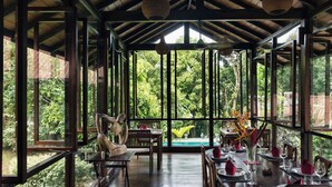 A dining area with a view of lush greenery, wooden furniture, and a pool in the background. - Rosyth Estate House (Pinnawala)