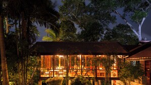A modern building with large glass windows, surrounded by lush greenery. - Rosyth Estate House (Pinnawala)