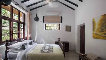 Un dormitorio con una cama grande, una ventana, un equipo de aire acondicionado, un banco de madera y un cuadro en la pared.