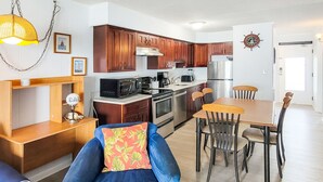 Een moderne keuken met houten kastjes, roestvrijstalen apparatuur en een eethoek met een blauwe stoel en een houten tafel.