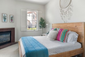 Un dormitorio con una cama de madera, colcha azul, atrapasueños y una ventana con persianas.