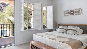 Ein Schlafzimmer mit einem großen Bett, einer hölzernen Bank und Blick auf einen Balkon mit Geländer.