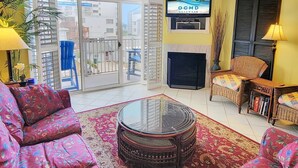 Un soggiorno con televisore che mostra 'OCMD GETAWAYS', un caminetto, un balcone con vista sugli edifici e un tappeto decorato.