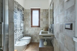 A bathroom with a toilet, bidet, and sink, tiled walls, and a window.