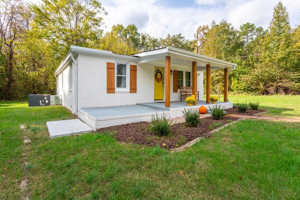 A single-story house with a porch, a front door with a wreath, and a small garden with a pumpkin.