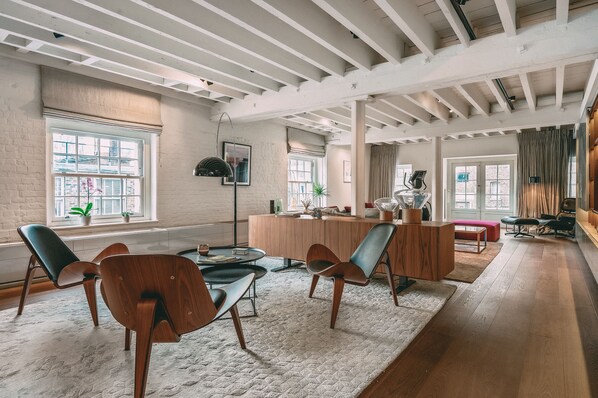 A spacious living room with a wooden floor, a large window, and a modern kitchen area.