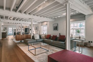 A spacious living room with a sectional sofa, a glass coffee table, and a red ottoman.