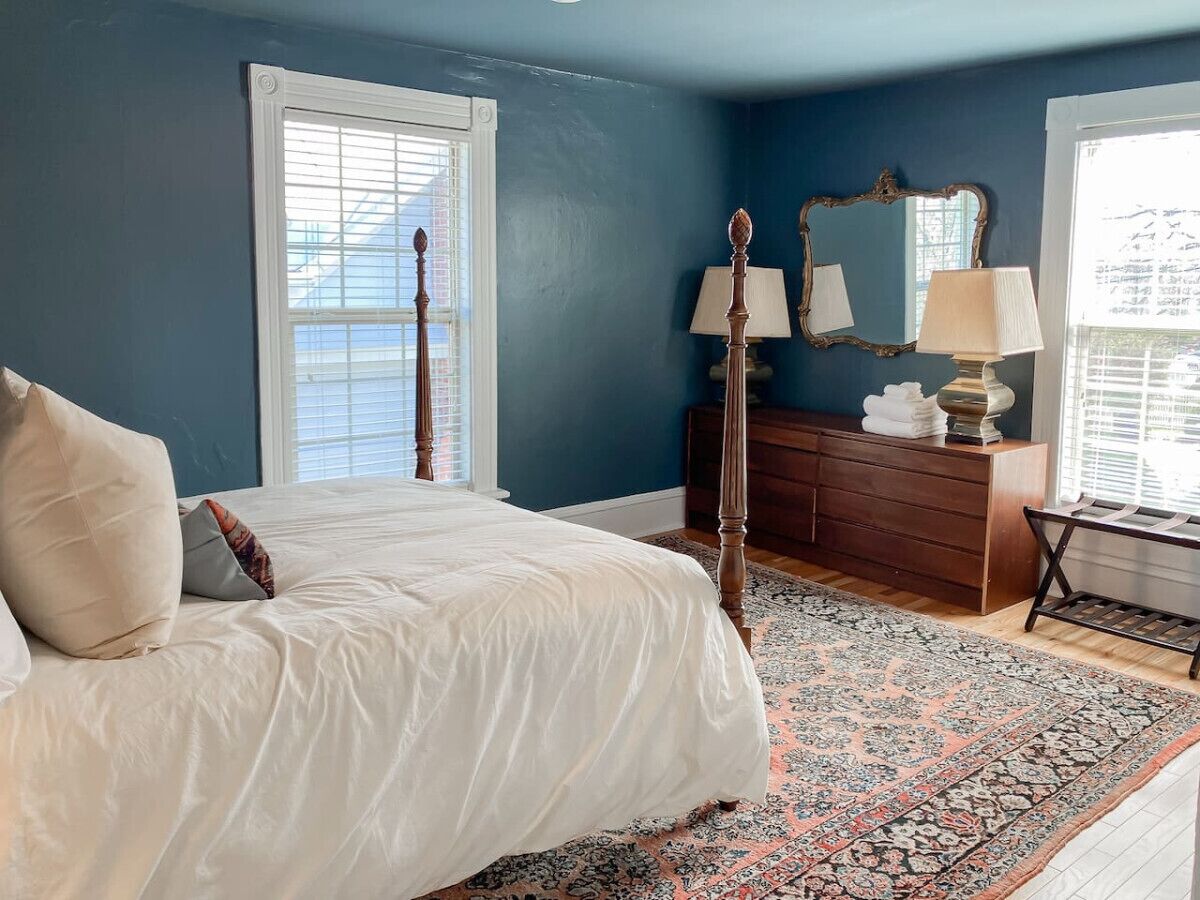 A bedroom with a bed, dresser, mirror, and a patterned rug.