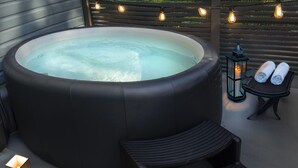 Ein Whirlpool mit einer Holterrasse, zwei Liegestühlen und einer Laterne.