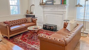 Ein Wohnzimmer mit braunen Ledersitzmöbeln, einem runden Couchtisch, einem Kamin und einem roten Teppich mit Muster.