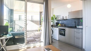 Une cuisine moderne équipée d’un four encastré, d’une machine à café et d’un évier. Une porte-fenêtre coulissante donne accès à un balcon avec vue sur la rue.