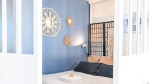 Une chambre à coucher comprenant un lit, une table de chevet, une lampe fixée au mur et des œuvres d’art décoratives accrochées au mur.