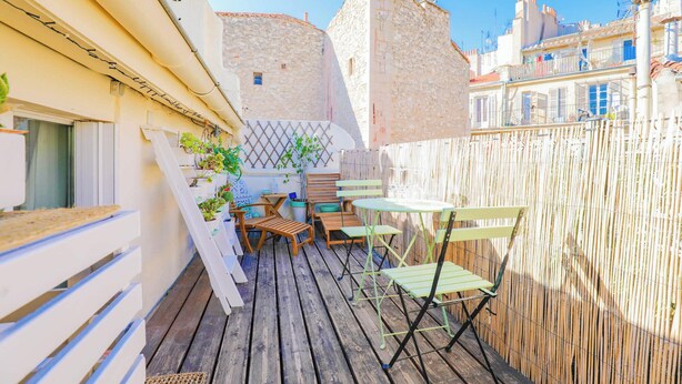 A wooden deck with outdoor furniture, a bamboo fence, and stone buildings in the background.