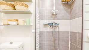 A bathroom with a toilet, a shower with a handheld showerhead, and shelves with baskets and toiletries.