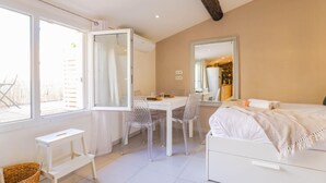 A modern bedroom with a large bed, a dining table with chairs, a small white desk, and a large mirror.