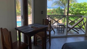 Ein Zimmer mit einem Balkon, der Blick auf einen Strand bietet, mit einem Tisch und Stühlen, sowie eine Aussicht auf Palmen und das Meer.