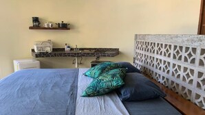 Ein Bett mit grauer und weißer Bettdecke, zwei Kissen, ein Holz-Kopfstück und ein Badezimmer mit Waschbecken und Regalen.