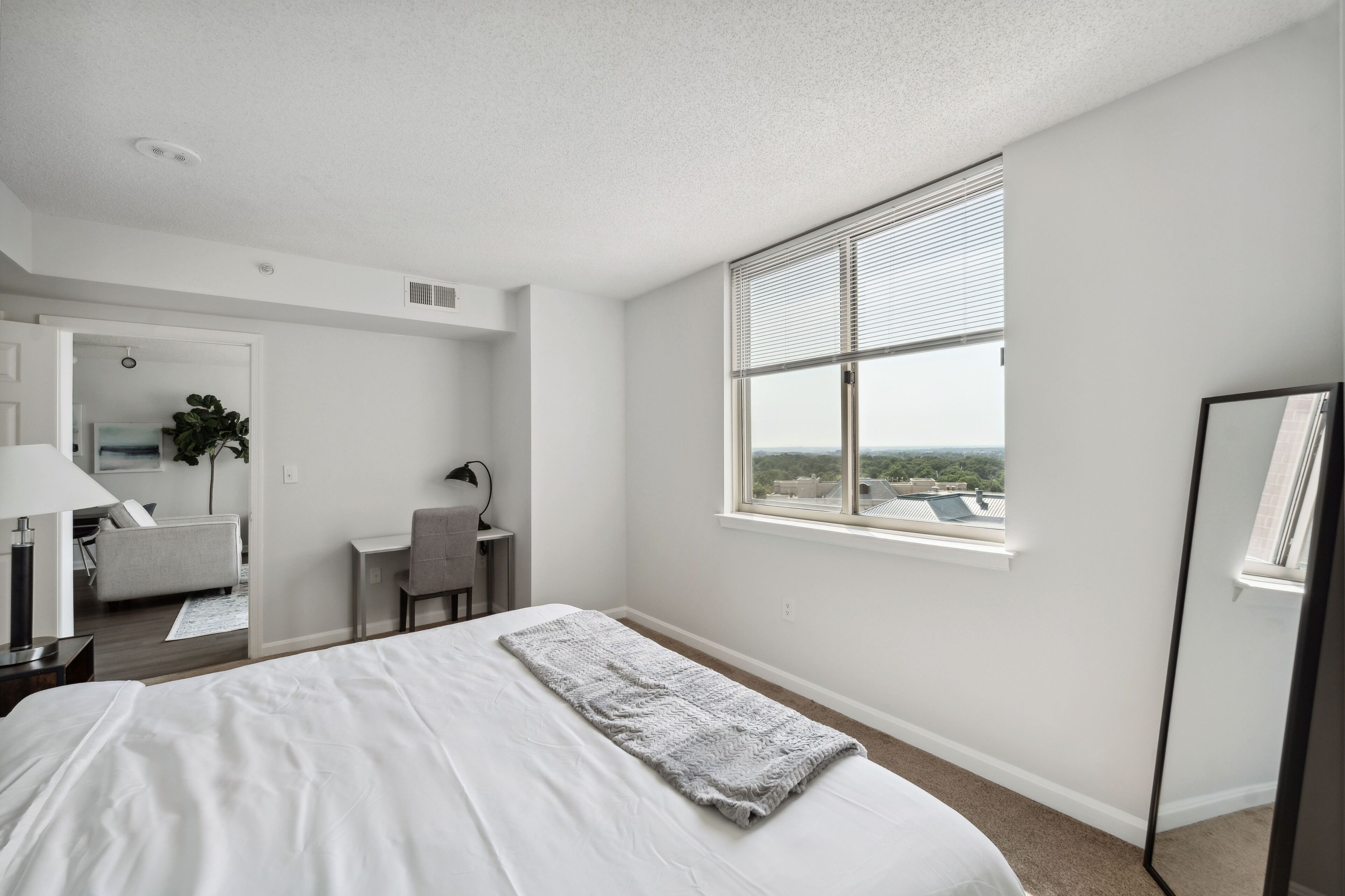 A modern hotel room with a large bed, a desk, a chair, and a window with a city view.