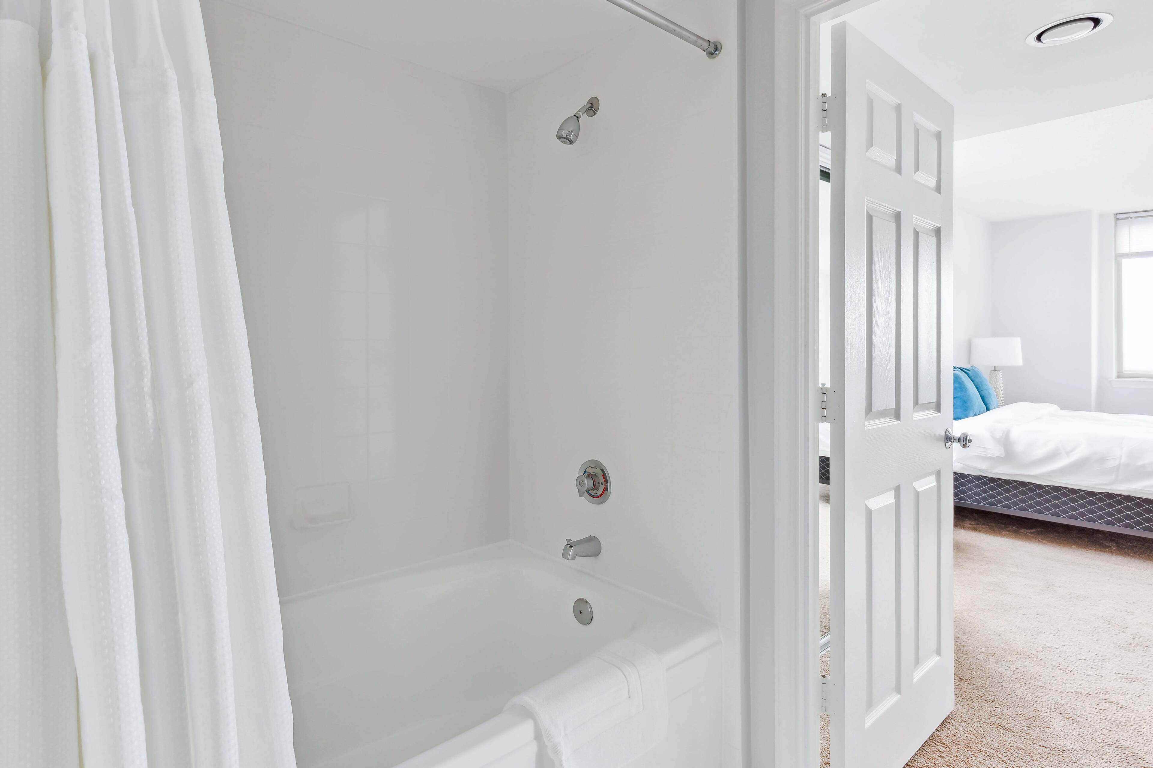 A modern bathroom with a bathtub, shower, and a white door leading to a bedroom.