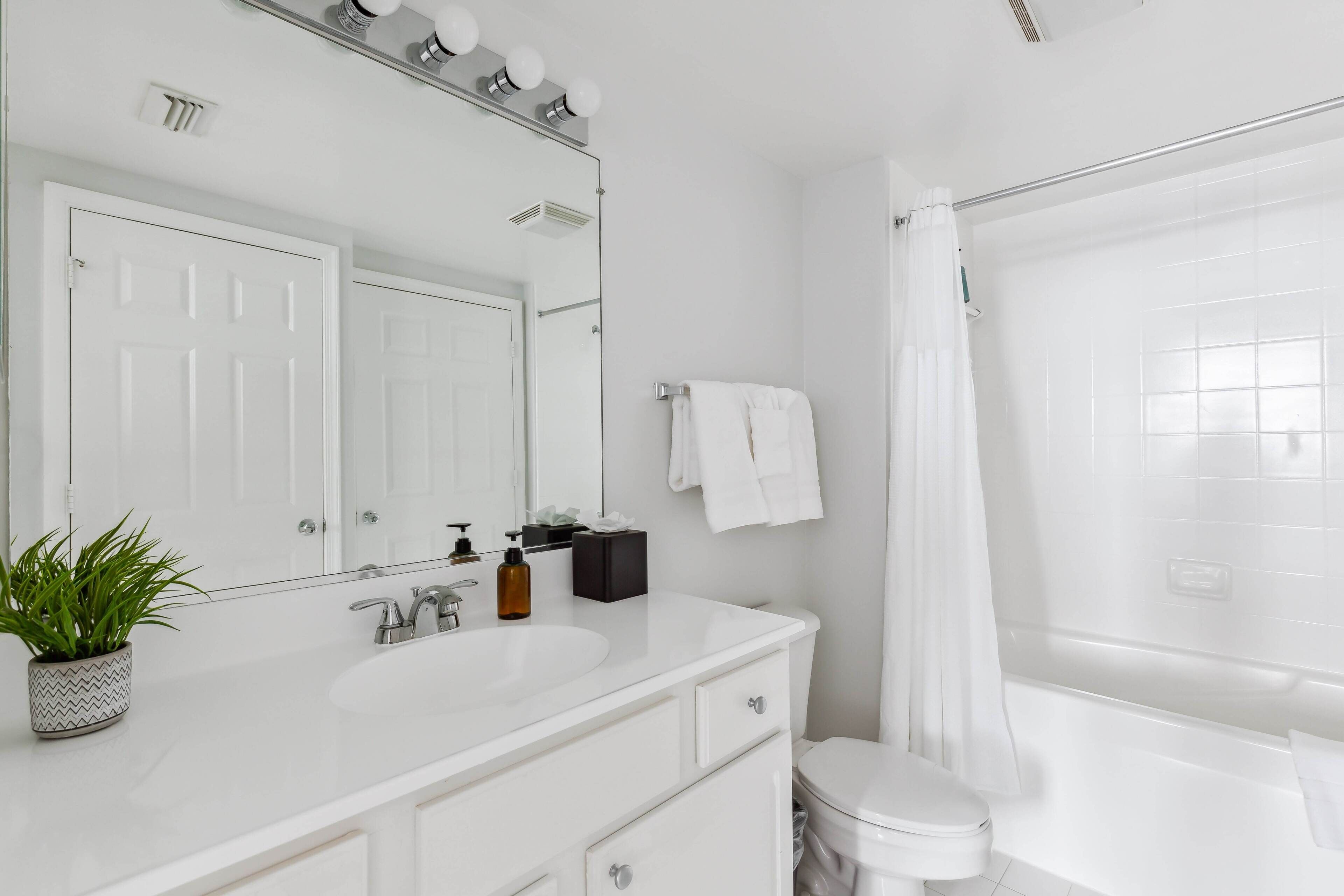 A modern bathroom with a white vanity, a large mirror, a sink, a toilet, and a shower with a curtain.